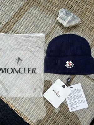 Mörkblå Moncler mössa  - Snygg mörkblå Moncler mössa i ribbstickad ull med klassisk logga framtill. Mössan har uppvikt kant och kommer med originalpåse och tags. Perfekt accessoar för kyliga dagar och ger en clean look till din outfit.https://code.moncler.com/?QR=35225294UPUY