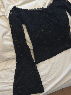 Svart spetsblus med vida ärmar - Säljer en svart blus i genombruten spets med blommönster. Toppen har långa, vida ärmar och en lätt croppad passform. Perfekt för dig som vill ha en statement topp med romantiska vibbar och snygga detaljer.