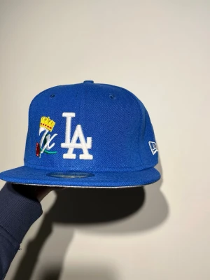 Blå LA Dodgers 59FIFTY keps New Era - Säljer en blå LA Dodgers 59FIFTY keps från New Era med broderade detaljer, inklusive LA-logga, krona och World Series Champions-text bak. Kepsen har rak skärm i grått och klassisk passform. Perfekt för dig som vill ha sportig stil.