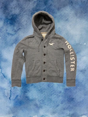 Vintage Hollister Cardigan Med Knappar - Säljer denna otroliga sällsynta och feta Hollister cardigan med knappar | Mycket bra skick, ett litet hål vid högra ärmen som knappast syns, se bild | Längd ≈ 64cm, Bredd armhåla - armhåla 53 cm | Modell 175, 68kg | PRIS KAN DISKUTERAS!