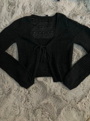 Svart stickad, mönstrad kofta med snörning - Säljer en svart stickad kofta med snyggt hålmönster och snörning framtill. Jättefint stickat mönster! Den är aldrig använd!