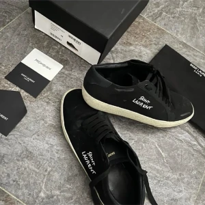 Svarta sneakers från Saint Laurent - Svarta sneakers från Saint Laurent med vit sula och tydlig logga på sidan. Skorna har snörning och rund tå, tillverkade i skinn med klassisk design. Perfekta för dig som gillar stilrena och lyxiga sneakers med en urban vibe.
