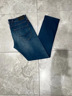 Replay Anbass jeans - Replay Anbass jeans i klassisk blå färg. Jeansen har dragledja och knapp framtill samt diskreta sömmar. Modellen är slim och tillverkad i mjukt bomullsmaterial med lite stretch för extra komfort. Perfekta för dig som gillar lite mer bekvämare och stiliga jeans. Storleken är i L34 och W31.