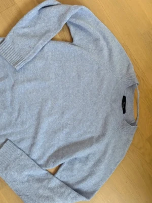 Ljusblå stickad tröja med rund hals - Mysig ljusblå stickad tröja med rund hals och ribbade muddar vid ärmslut och nederkant. Perfekt för kyliga dagar och enkel att matcha med jeans eller kjol. Klassisk och stilren design som passar till många olika looks.