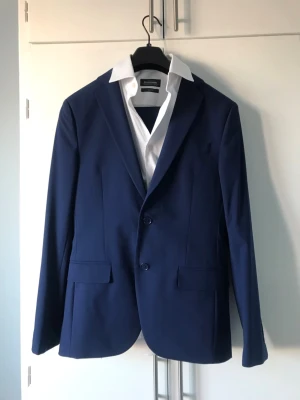 Kostym  + skjorta Dressmann - SLIM FIT kostym från Dressmann. En kavaj där vit skjorta och byxor till kavaj medföljer.   Strl på kavaj: 46 Regular  Strl på skjorta: 37/38 S Strl på kostymbyxor: 30/30  Enbart använd några timmar. 