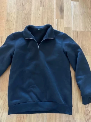 Svart fleece-tröja med half zip - Mysig svart fleece-tröja med halv dragkedja i halsen. Tröjan har en enkel och stilren design med långärmade ärmar och mjukt material som passar perfekt för kyliga dagar. Perfekt att slänga på sig när man vill vara både bekväm och snygg.