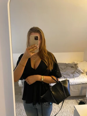 Svart omlottblus från SHEIN - Säljer en svart omlottblus från SHEIN i storlek XS. Blusen har v-ringning, korta vida ärmar och markerad midja som ger en snygg siluett. Perfekt att styla med jeans eller kjol för en trendig look.