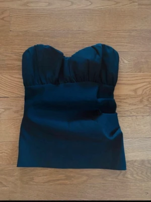 Svart  tubtopp från Zara - Snygg svart axelbandslös tubtopp med bandeau-formad överdel och lätt rynkade kupor.  Säljer pga att den tyvärr är för liten för mig 
