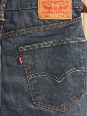 Levi's 527 blå jeans bootcut - Säljer ett par klassiska Levi's 527 jeans i blå tvätt med bootcut passform. Jeansen har snygga kontrastsömmar, fem fickor och det ikoniska röda Levi's-märket på bakfickan. Tillverkade i slitstarkt denimtyg som ger en skön känsla och grym look.
