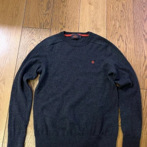Mörkgrå Morris tröjä - Snygg mörkgrå stickad tröja från Morris i 100% merinoull. Rund hals och långärmad modell med röd broderad logga på bröstet. Perfekt för dig som gillar stilrena och klassiska plagg med en twist. Passar dig som vill ha en mjuk och skön tröja med bra passform.  ! Fits better men S