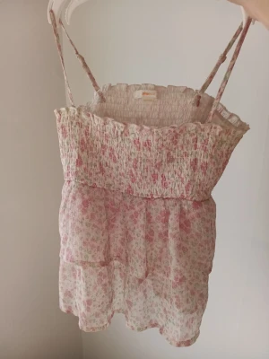 Blommig top från Gina Tricot - Supersöt topp med tunna justerbara axelband från Gina Tricot. ❤️Toppen har ett blommigt mönster i ljusrosa och vitt, samt två lager volanger nedtill som ger en luftig känsla. Perfekt för varma dagar,så passa på att köpa till sommaren till ett jättebra pris. 45 kr+frakt🌸🌷