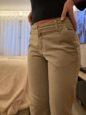Snygga beige byxor – tidlös och smickrande passform - Stilrena beige byxor i klassisk modell som passar perfekt till både vardag och jobb. Innerbenslängd är 85 cm men dom är uppsprättade (se bild) Byxorna har en rak/smal passform med hög midja som sitter snyggt och är enkla att matcha med både toppar, skjortor och stickat. En garderobsklassiker som aldrig går ur stil! Färg: Beige / sand. Stil: Klassisk, minimalistisk, elegant. Passform: Rak / smal. Skick: Mycket fint skick