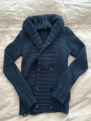 Mörkblå stickad kofta Massimo Dutti - Säljer en mörkblå stickad kofta från Massimo Dutti i storlek M. Koftan har bred krage, dubbelknäppning med svarta knappar och ribbade detaljer längs kragen och framstycket. Perfekt för kyliga dagar och enkel att matcha med jeans eller kjol.