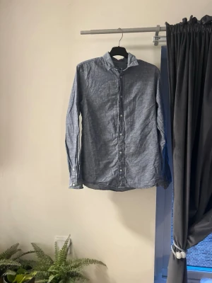 Blå skjorta från Jack & Jones - Säljer en stilren blå skjorta från Jack & Jones med klassisk krage och vita knappar. Skjortan är långärmad och har en avslappnad passform. Perfekt till jeans eller chinos för en clean look.