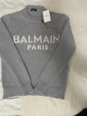 Grå stickad tröja - Snygg grå stickad tröja med vit logotyptext framtill. Den utger sig vara storlek S men är M - L. Materialet är mjukt och ger en skön känsla. Hör av dig vid intresse, pris kan diskuteras!