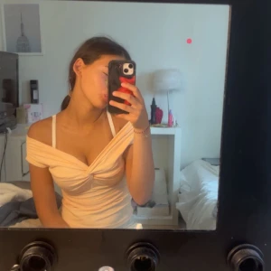 Aprikos offshoulder topp med twist - Säljer en ljusbeige offshoulder topp med snygg twist-detalj framtill. Toppen är figurnära och har en croppad känsla, perfekt för dig som gillar trendiga och feminina plagg. Materialet är mjukt och stretchigt, vilket gör den bekväm att bära.