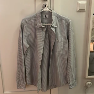 Randig skjorta från NN07 - Snygg randig skjorta från NN07 i vitt och blått. Klassisk krage, bröstficka och knäppning framtill. Långärmad modell i mjuk bomull, perfekt för en clean och stilren look.