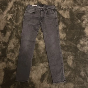 Svarta Replay jeans slim fit - Säljer ett par svarta jeans från Replay med klassisk femficksdesign och smal passform. Jeansen har diskreta slitningar och snygga detaljer på bakfickorna. Perfekta för dig som gillar en stilren och modern look. Strlk 32/32