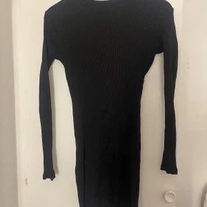 Svart ribbad långärmad klänning - En svart, ribbad klänning med lång ärm och kroppsnära passform. Klänningen har en enkel och stilren design, är knälång och tillverkad i ett stretchigt material som sitter snyggt på kroppen. Perfekt för dig som gillar minimalistisk stil och vill ha något som är både bekvämt och trendigt.