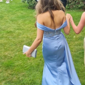 Ljusblå balklänning med spets - Säljer en ljusblå balklänning med offshoulder och slits framtill. Överdelen har vackra spetsdetaljer och pärlor, samt en markerad midja med drapering. Kjolen är i satinliknande material och faller snyggt. Perfekt för bal eller student!