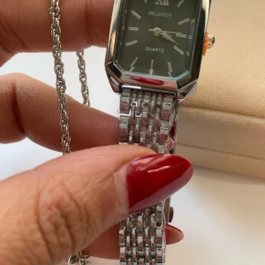 Silvrig klocka från Irlandy med länk - Stilren klocka från Irlandy med rektangulärt svart urtavla och silverfärgad länk i metall. Klockan har tydliga indexmarkeringar och romersk tolvmarkering. Klassisk design som passar till många stilar.