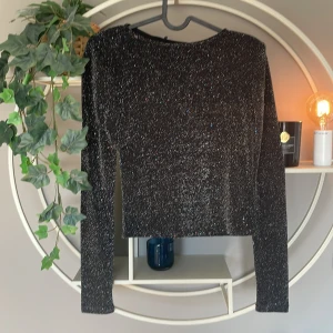 Glittrig svart topp från Bik Bok XS - Snygg svart långärmad topp från Bik Bok i storlek XS. Toppen är glittrig med inslag av små färgade glittertrådar som ger en festlig känsla. Modellen är croppad och har en rund halsringning. Perfekt för dig som vill sticka ut med stil. Även vaderad i axlarna vilket ger en snygg look. Perfekt till lite festligare dagar och utmärkt till nyår. Helt ny aldrig använd. 