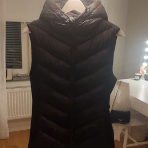 Svart dunväst  - Svart dunväst från Zara med huva och snyggt quiltat mönster. Västen har en stilren look och är perfekt för lager-på-lager. Passformen är normal och materialet är mjukt och värmande.