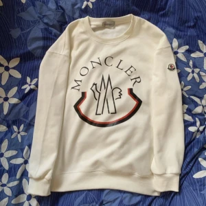 Moncler sweatshirt/ hoodie vit - Säljer en clean vit sweatshirt från Moncler med stor tryckt logga på bröstet och klassisk patch på ärmen. Tröjan har rund halsringning och långa ärmar, perfekt för dig som gillar stilrena märkesplagg.