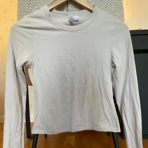 Beige långärmad tight tröja  - En enkel och stilren beige långärmad tröja från H&M. Tröjan har rund halsringning och är gjord i mjuk bomull, perfekt för att bygga lager eller bära som den är. Passformen är tight. 