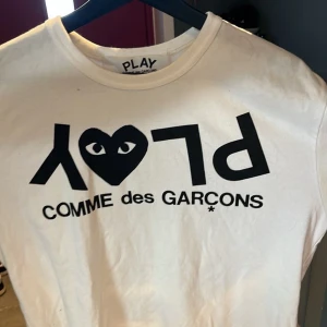Vit Comme des Garçons Play t-shirt XL - Säljer en vit t-shirt från Comme des Garçons Play i storlek XL. T-shirten har det ikoniska svarta PLAY-trycket med hjärta och ögon på bröstet. Klassisk rund hals och korta ärmar. Tillverkad i mjuk bomull för skön passform. Dock så sitter den mer som M-L då den är liten i passform.