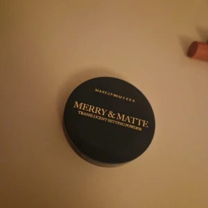 Setting Powder - Translucent setting powder från Makeup Mekka i en rund, kompakt burk med svart och blågrön plast. Ger en matt finish och håller sminket på plats hela dagen. Perfekt för att fixera foundation och concealer utan att kännas tung på huden.