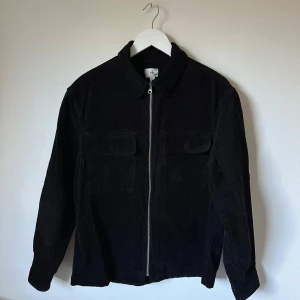 Svart manchesterjacka från H&M - Svart manchesterjacka från H&M i storlek M. Jackan har klassisk krage, två stora bröstfickor med lock och stängs med dragkedja framtill. Tillverkad i 100% bomull och har långa ärmar. Perfekt för dig som gillar stilren och enkel look. 3P8