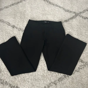 Svarta kostymbyxor från BikBok - Svarta kostymbyxor från BikBok i modellen Vera, lite utsvängda längst ner. Byxorna har diskreta bakfickor och är tillverkade i ett slätt tyg som ger en stilren look. 