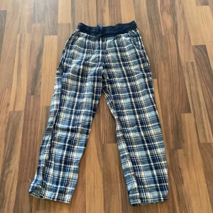 Blårutiga mjukisbyxor från Kappahl - Blårutiga mjukisbyxor från Kappahl med resår och snörning i midjan. Byxorna har ett klassiskt rutmönster i blått och vitt, raka ben och är tillverkade i mjukt bomullstyg. Perfekta för chill dagar hemma. Priset kan förhandlas vill bara få dem sålda