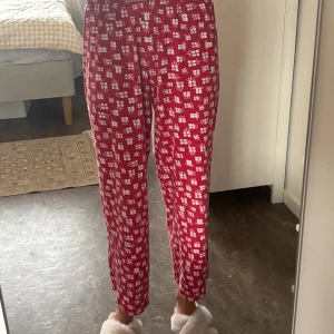 Röda pyjamas med julklappsmönster - Röda mjukisbyxor med vita julklappar som mönster. Byxorna har elastisk midja och är raka i modellen, perfekta för att chilla hemma under vintern. Mjukt och skönt material som känns riktigt cozy.