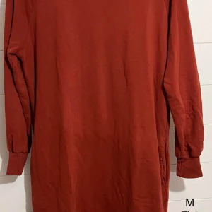 Roströd långärmad bomullsklänning - Enkel och snygg roströd klänning i bomull med lång ärm och rund hals. Modellen är rak och avslappnad, perfekt för dig som gillar en stilren look. Klänningen har muddar vid ärmsluten och är i en mjuk, skön kvalitet.