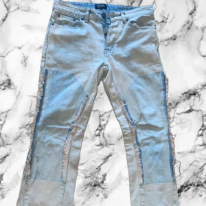 Ljusblå jeans med slitna detaljer - Unika ljusblå jeans från BOHOOMAN med råa, slitna detaljer längs benen och patchade partier. Klassisk femficksmodell med normal passform och raka ben. Perfekta för dig som gillar en edgy streetstil och vill sticka ut.