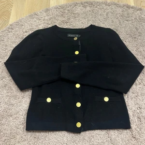 Svart kofta från Stockh LM med guldknappar - Snygg svart kofta från Stockh LM med rund halsringning och dekorativa guldknappar framtill. Koftan har två små fickor framtill och är långärmad. Säljer en mörkblå och rosa också! Bättre bilder finns om man ber om det! 