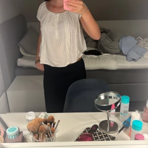 Vit blus med spets och knappar - Söt vit blus med korta ärmar, rund halsringning och dekorativa spetsdetaljer framtill. Blusen har små knappar längs bröstet och en luftig, loose passform som ger en avslappnad vibe. Perfekt att styla med jeans eller kjol för en fräsch look.