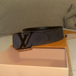 Louis Vuitton bälte grå/svart - Hej! Jag säljer mitt Louis Vuitton bälte med klassiskt monogrammönster och stor LV-logga i metall. Bältet är köpt i louis vuttion affären i stockholm för 5850kr och den har en mörk design som passar perfekt till jeans eller kostymbyxor. Det finns vissa tecken på användning som jag försökte få med i bilderna men ingen har märkt det när den har suttit på mig. Det här bältet ger dig en bra outfit oavsett vad du har för skor eller jacka. Hör av dig gärna så kan vi diskutera mer!