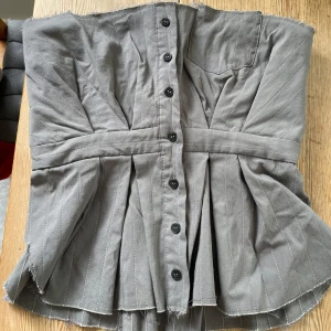 Korsett-topp - Korsett-topp med insydd ”bh-del”.  Insidan stängs med hyskor. Knapparna framtill gör den något liten i storleken. Endast använd vid ett tillfälle.