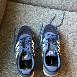 Blå adidas sneakers strl 42 - Snygga blå adidas sneakers med klassiska vita ränder på sidorna och beige sula. Skorna är helt nya och inte använda! Vid frågor och funderingar är det bara att skriva. Vid fler bilder kring skorna så finns jag alltid tillgänglig! 