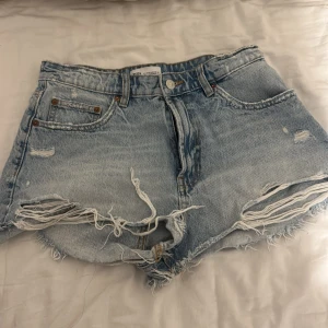Ljusa jeansshorts från Zara - Säljer ett par ljusblå jeansshorts från Zara med råa, fransiga kanter och slitna detaljer framtill och baktill. Mid/ high waist använt få gånger 