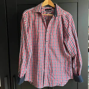 Rutig skjorta i rött, blått och vitt - Snygg rutig skjorta i rött, blått och vitt med kontrastfärgade mörkblå manschetter och krage. Skjortan har klassisk krage, knäppning framtill och långa ärmar. Perfekt för dig som gillar en färgstark och stilren look.