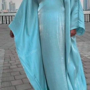 Ljusblå abaya  i satin - Säljer en elegant ljusblå abaya i glansigt satinmaterial. Klänningen har vida ärmar och en rak, loose passform som ger en flowy känsla. Perfekt för dig som vill sticka ut med en stilren och modern look.