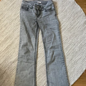 Grå bootcut jeans från Nelly - Snygga grå jeans från Nelly med bootcut passform och låg midja. Stitch jeans. Jeansen har svarta broderade detaljer på bakfickorna och dubbla knappar framtill. Tillverkade i klassiskt denimtyg med en cool tvättad look. Fint skick, de ända är den vita ”fläcken” eller vad man ska säga på insida lår men inget jag tycker man tänker på när man har den på sig. Slutsålda! Strl 34 men Passar 34/36