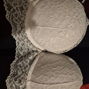 Vit spetsig bandeau tubtopp - Säljer en vit super push up bh med vacker blommig spets och vadderade kupor. Toppen har axelband  och har en romantisk känsla med sina detaljerade spetskanter. 