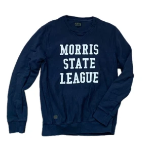 Mörkblå sweatshirt från Morris, M - Snygg mörkblå sweatshirt från Morris med vit text 'Morris State League' på bröstet. Tröjan har rund hals, långa ärmar och är gjord i mjuk bomull. Perfekt för dig som gillar college-vibe och sportig stil.