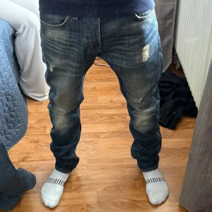 Mörkblå jeans med slitningar - Säljer ett par mörkblå jeans med snygga slitningar och tvättade detaljer. Jeansen har klassisk femficksdesign och rak passform. Storlek 30/32. Passar 180-185 och dig som väger 65-75