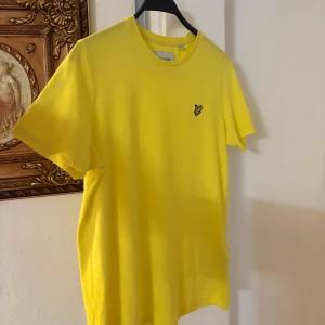 Gul t-shirt från Lyle & Scott S - Fräsch gul t-shirt från Lyle & Scott i ekologisk bomull. Klassisk passform med rund hals och korta ärmar. På bröstet sitter den ikoniska broderade fågel-loggan. Perfekt för dig som vill sticka ut med färg och stil.